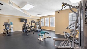 Ein Fitnessraum mit unterschiedlichen Trainingsgeräten, einem Wasserspender und einem Fernseher an der Wand.