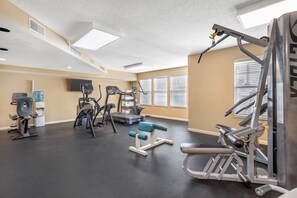 Ein Fitnessraum mit unterschiedlichen Trainingsgeräten, einem Wasserspender und einem Fernseher an der Wand.