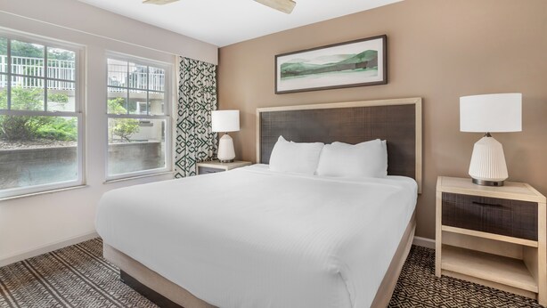A hotel room with a large bed, two bedside tables with lamps, a ceiling fan, a window with a view of greenery, and a framed picture on the wall. - 2BR Getaway Minutes from Dollywood (Pigeon Forge)