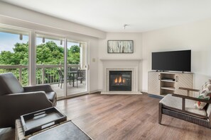 Ein Wohnzimmer mit Kamin, Fernseher und einem Balkon mit Gartenmöbeln.