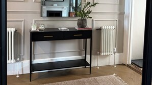 Ein Raum mit einer schwarzen Konsole, einem Spiegel, einem Kamin und einer Heizung.