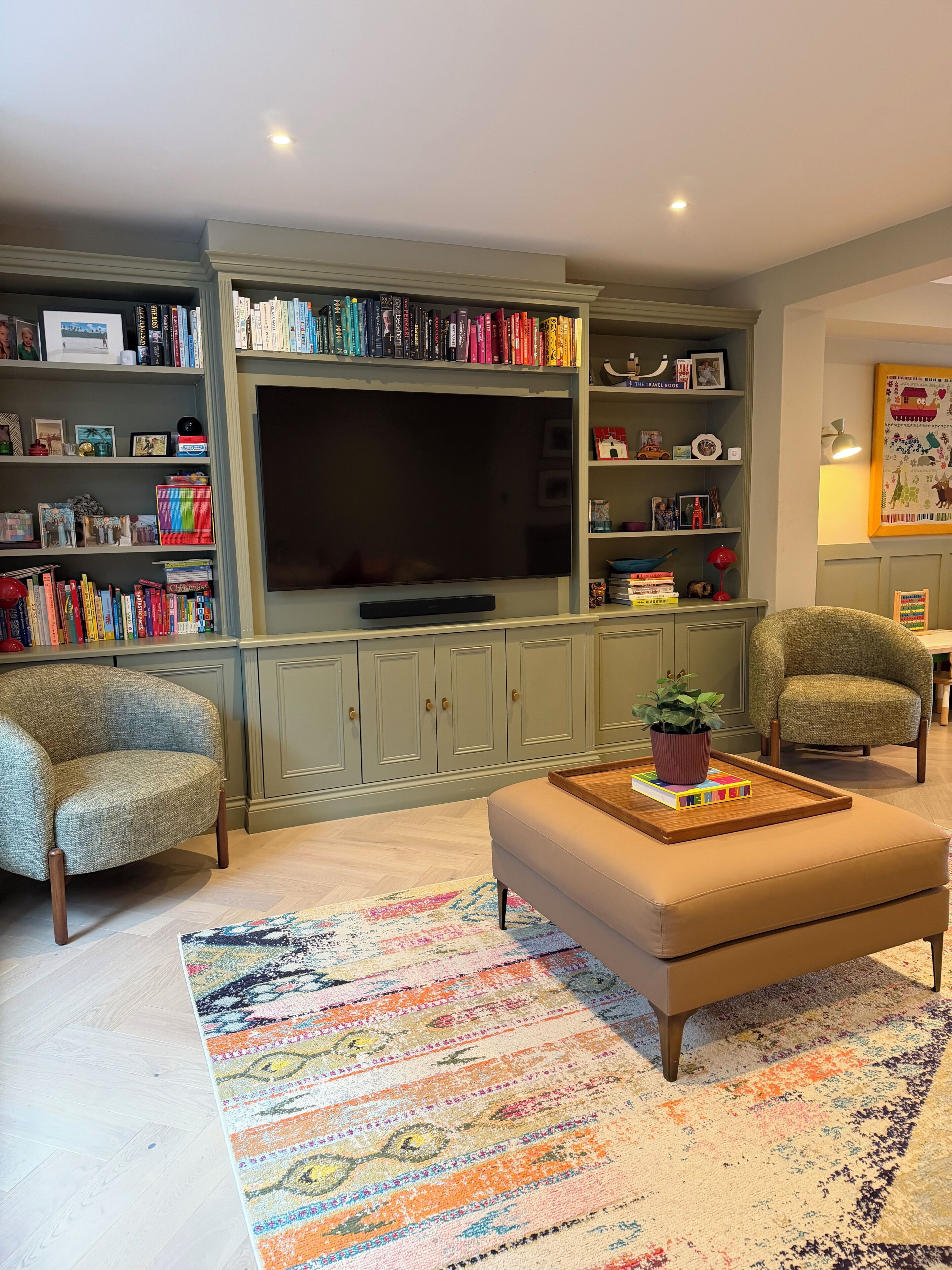 Un salon comprenant un téléviseur, des étagères à livres, deux fauteuils, une table basse et un tapis coloré.