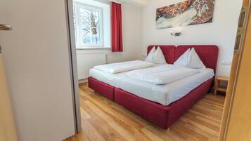 Un dormitorio con cama, ventana con cortinas, radiador y un cuadro en la pared.