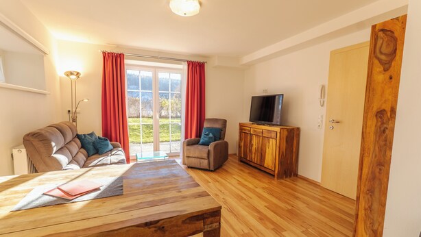 Uma sala de estar moderna com uma mesa de madeira, um sofá, uma televisão em um armário de madeira e uma porta de vidro deslizante para um jardim.