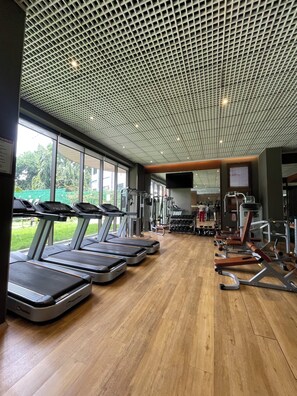 Et fitnesscenter med løbebånd, styrkemaskiner og et stort vindue med udsigt til grønne omgivelser.