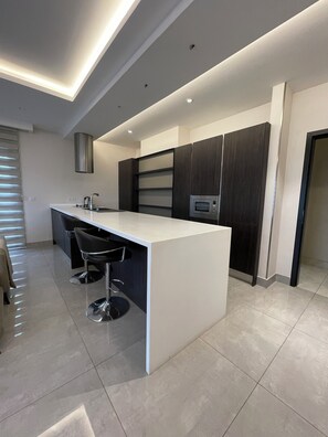 A modern kitchen with a central island, bar stools, a built-in oven, and a dark wood cabinet. - Luxury 2-Bedrooms Apartment in Airport Residential (Accra)