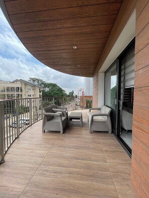 A balcony with wicker furniture, a tiled floor, and a view of the street and buildings. - Luxury 2-Bedrooms Apartment in Airport Residential (Accra)
