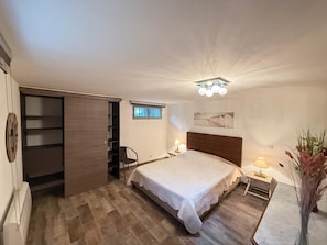 Ein Schlafzimmer mit Bett, Schrank, Nachttisch, Lampe und einem kleinen Fenster.