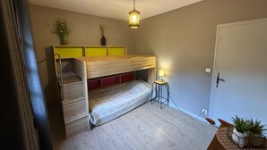 Ein kleines Zimmer mit einem Etagenbett, einem Nachttisch mit Lampe, einem Blumentopf und einer Tür.