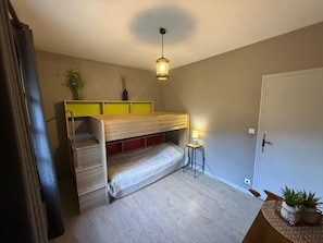 Ein kleines Zimmer mit einem Etagenbett, einem Nachttisch mit Lampe, einem Blumentopf und einer Tür.