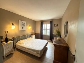 A bedroom with a bed, bedside tables, a dresser, a window with curtains, wall-mounted lights, and a framed picture. - Air-conditioned villa with a pool at the foot of the Luberon (Mérindol)