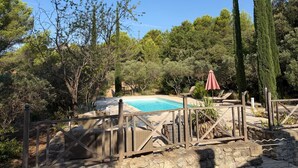 Ein Pool, umgeben von einem Holenzaun, mit einem roten Sonnenschirm und Liegestühlen in der Nähe.