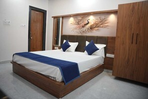 A bedroom with a wooden bed frame, a large mirror above the bed, and a wardrobe to the right. - Hotel Mayur Palace (Pushkar)