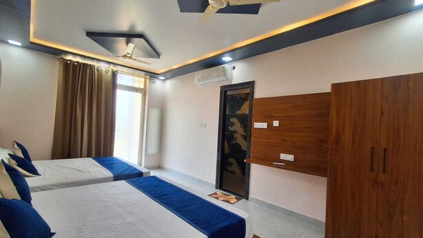 A hotel room with two beds, a wardrobe, a ceiling fan, and a window with curtains. - Hotel Mayur Palace (Pushkar)
