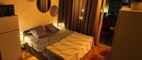 A hotel room with a bed, a refrigerator, a microwave, and a view of the outside.