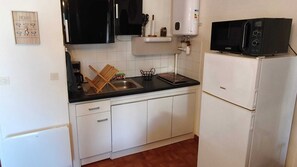 Eine kompakte Küche mit weißen Schränken, einer schwarzen Arbeitsplatte, einer eingebauten Mikrowelle und einem kleinen Kühlschrank.