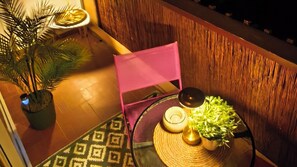 Ein Blick in den Raum zeigt einen strukturierten Boden, einen Blumentopf, einen pinken Sessel, einen kleinen runden Tisch mit Kerze und Pflanze darauf.