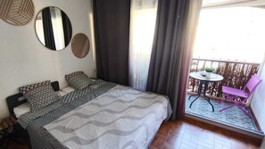 A bedroom with a bed, two pillows, a bedside table, and a window with curtains. - Studio Soleil Bleu - Within walking distance of the Port Plages Center (Agde)