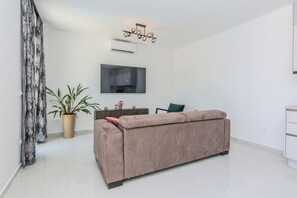 Ein modernes Wohnzimmer mit einer Couch, einem Topf mit Pflanze, einem Flachbildfernseher und einer Deckenleuchte.