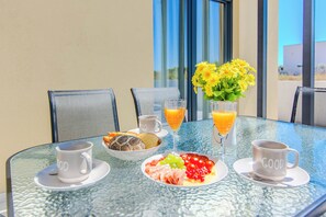 Een ontbijttafel met een bord eten, twee glaasjes sinaasappelsap, een kop koffie en een vaas gele bloemen.