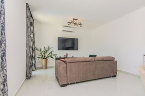 A modern living room with a sofa, a potted plant, and a flat-screen TV mounted on the wall. - Villa Caelora-Private Villa With Pool-Pet Friendly (Privlaka)