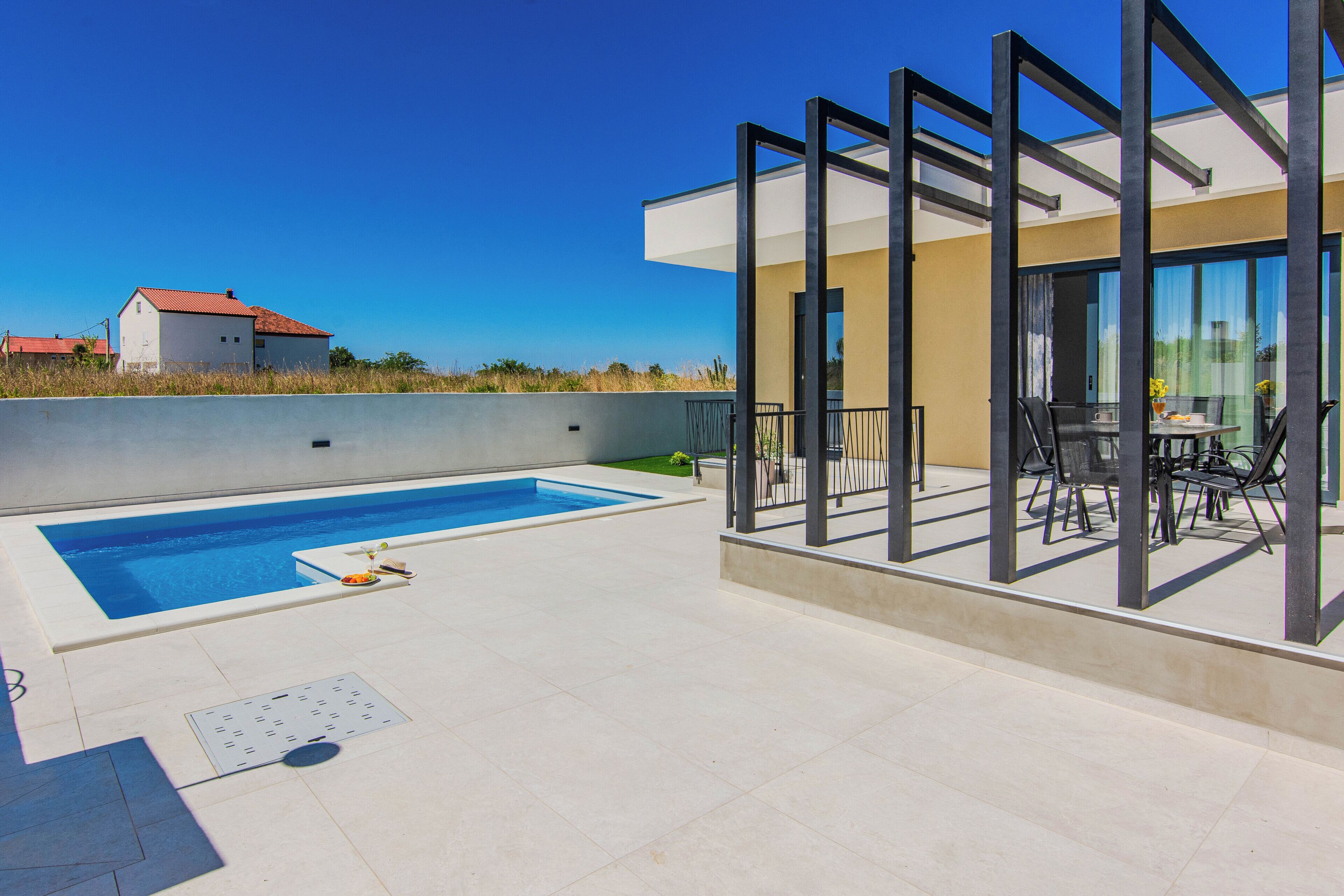 A modern outdoor pool area with a glass-enclosed patio and a view of a residential building in the background.
