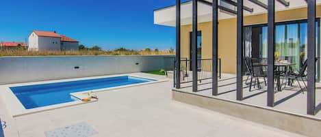 A modern outdoor pool area with a glass-enclosed patio and a view of a residential building in the background.