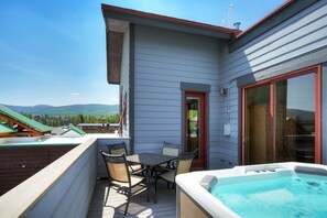 Een balkon met een jacuzzi, een tafel met stoelen en uitzicht op bergen.