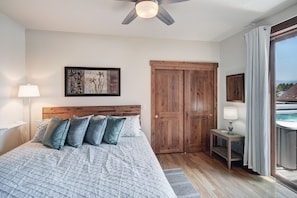 A bedroom with a bed, a wooden headboard, a nightstand with a lamp, a painting on the wall, a sliding door, and a view of a hot tub outside. - RARE One Bedroom Condo w/Private Hot Tub on Main Street (Frisco)