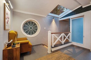 Un interior moderno con un sillón amarillo, un ventanal decorativo redondo y una escalera con una puerta azul.