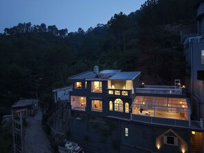 Una casa de varios pisos con numerosas ventanas y un balcón, rodeada de árboles.