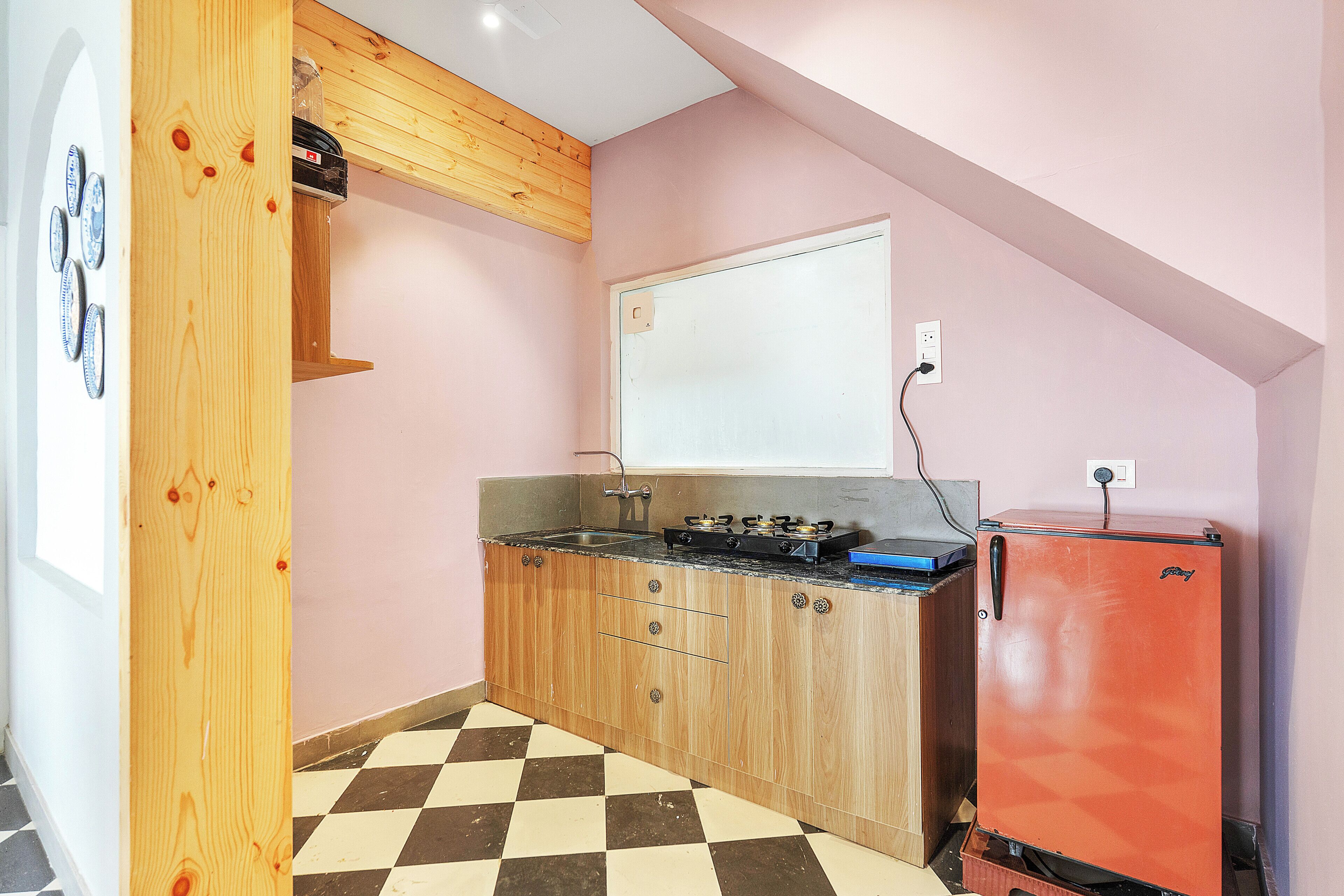 Una cucina compatta con mobili in legno, un fornello a gas, un frigorifero rosso e un pavimento a scacchi.