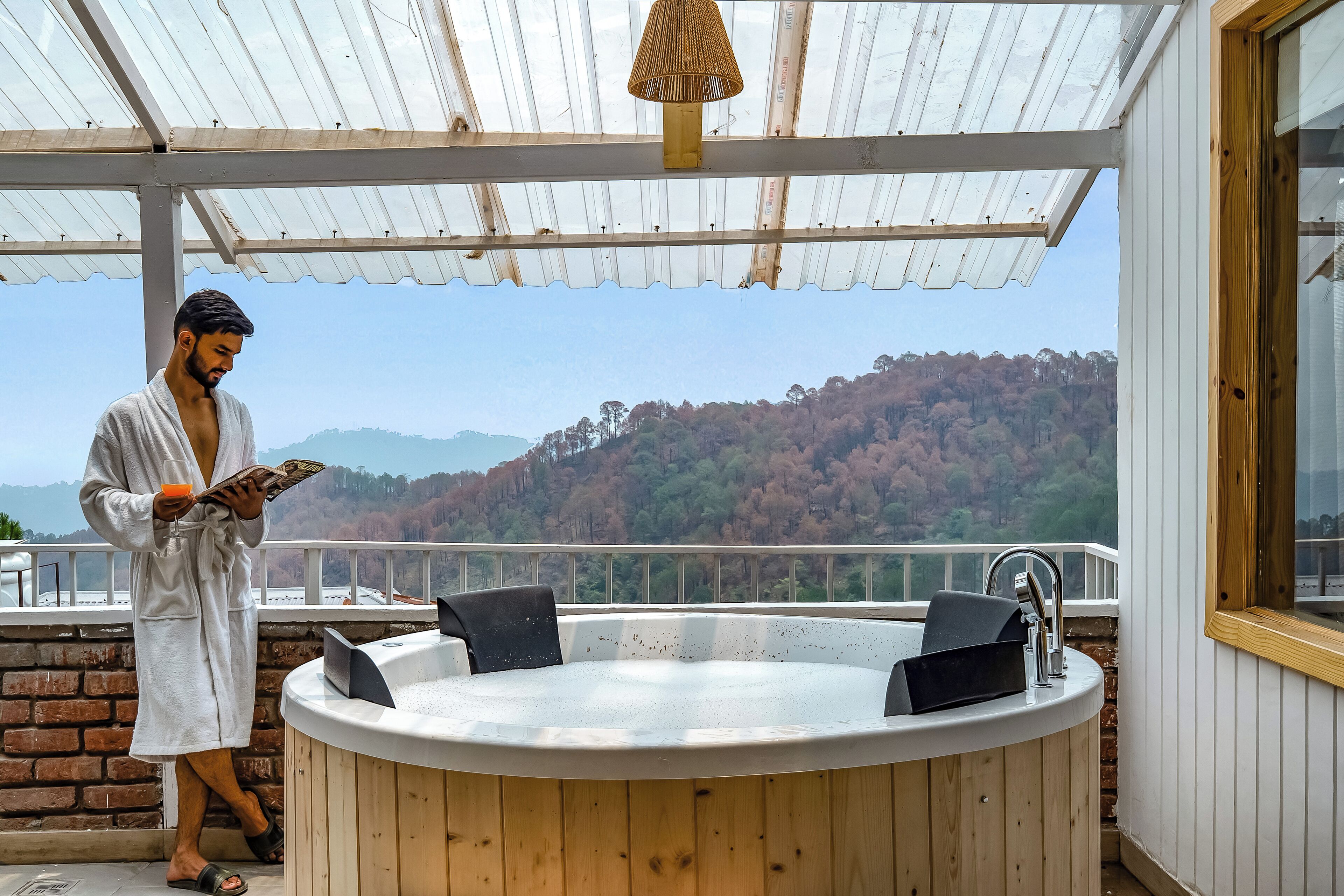 Iemand in een badjas staat bij een hottub met uitzicht op een bebost heuvel.'