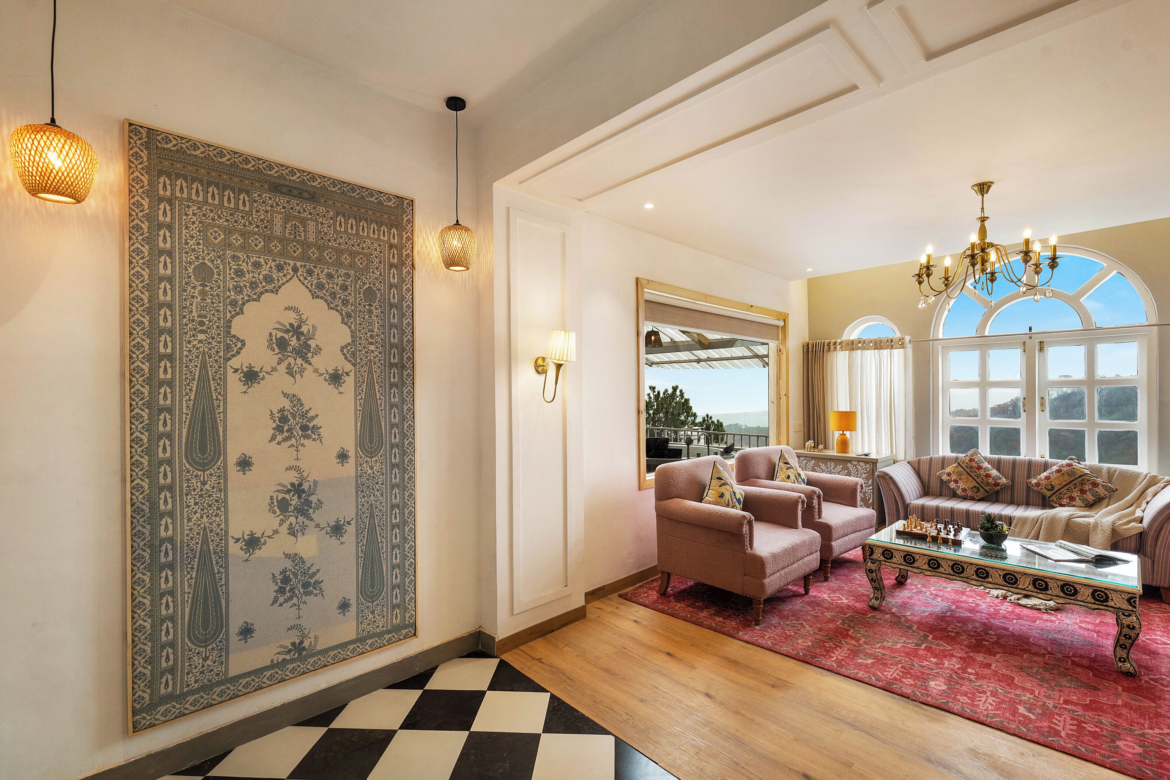 A spacious living room with a large patterned rug, a chandelier, and a view through a window.