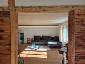 Ein gemütliches Wohnzimmer mit Holzbalkendecke, einem grauen Sofa und einem kleinen Tisch.
