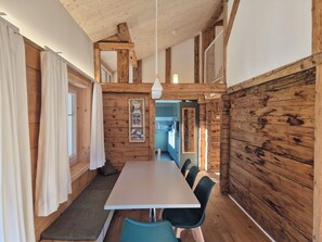 A wooden interior with a long table and chairs, a staircase, and a kitchen visible in the background. - Tgèsa Stefania, (Camischolas), by Interhome (Camischolas)