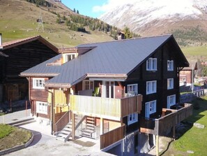A two-story wooden chalet with a balcony, a staircase, and a view of a mountainous landscape. - Tgèsa Stefania, (Camischolas), by Interhome (Camischolas)