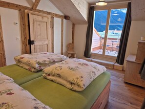 Une chambre avec deux lits, une armoire en bois, une chaise et une vue sur les montagnes par la fenêtre.