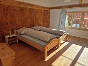 Ein hölzernes Bett in einem Zimmer mit Fenster, einem Nachttisch und einem Beistelltisch.