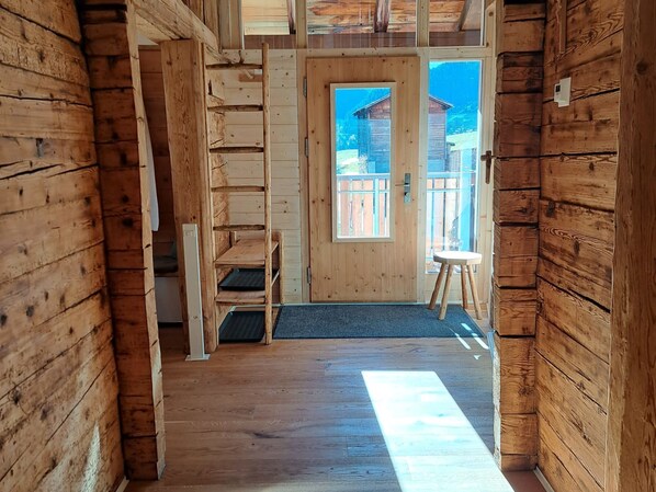 Un intérieur en bois avec une porte donnant sur l’extérieur, un petit tabouret et un banc.