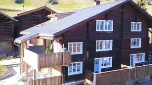 A multi-story wooden building with balconies, set against a mountainous backdrop.