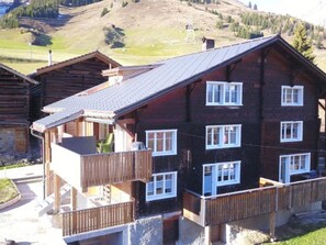 A multi-story wooden building with balconies, set against a mountainous backdrop. - Tgèsa Stefania, (Camischolas), by Interhome (Camischolas)