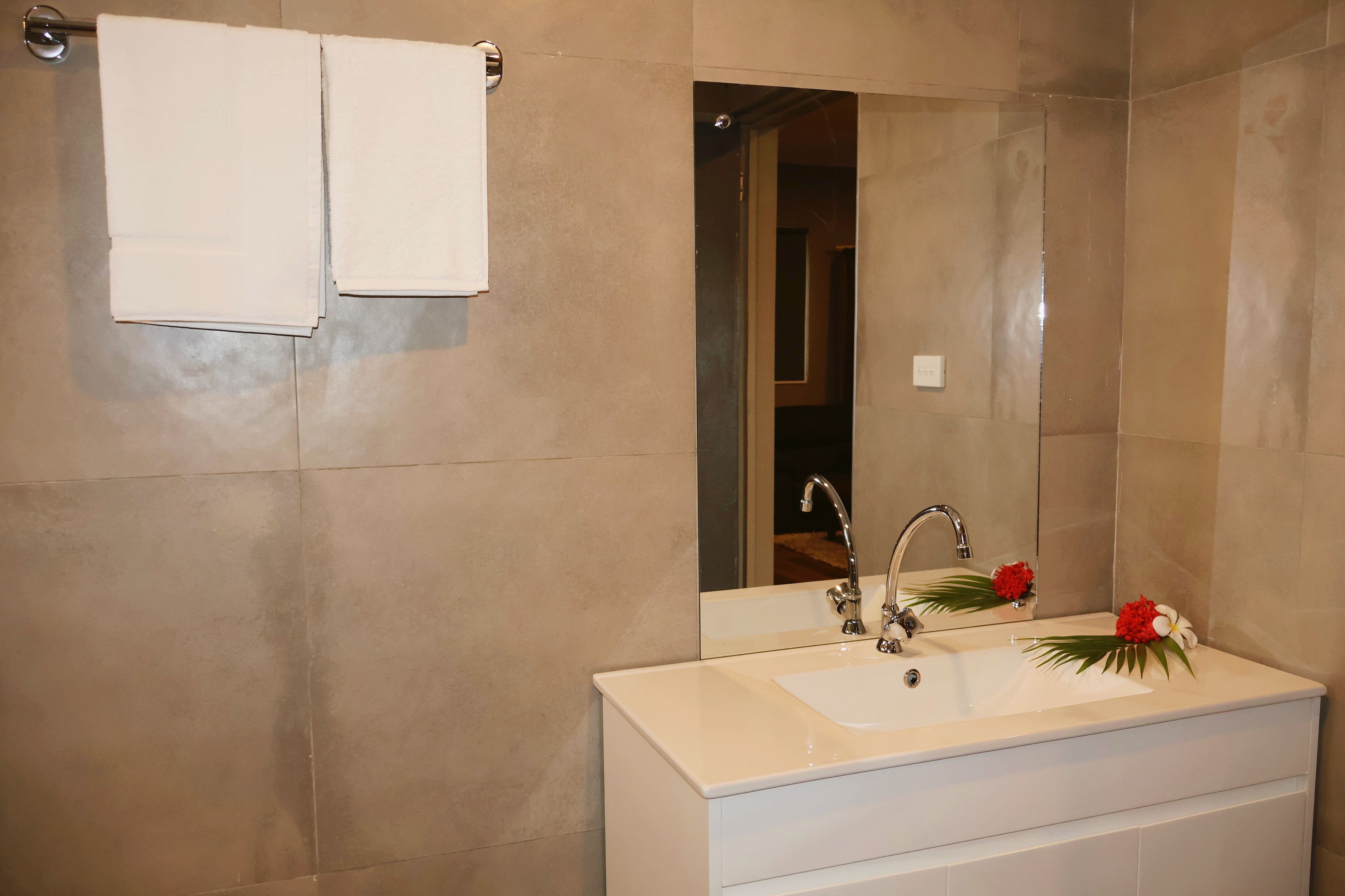 A bathroom with a white sink, two faucets, a mirror, and a towel rack with two towels.