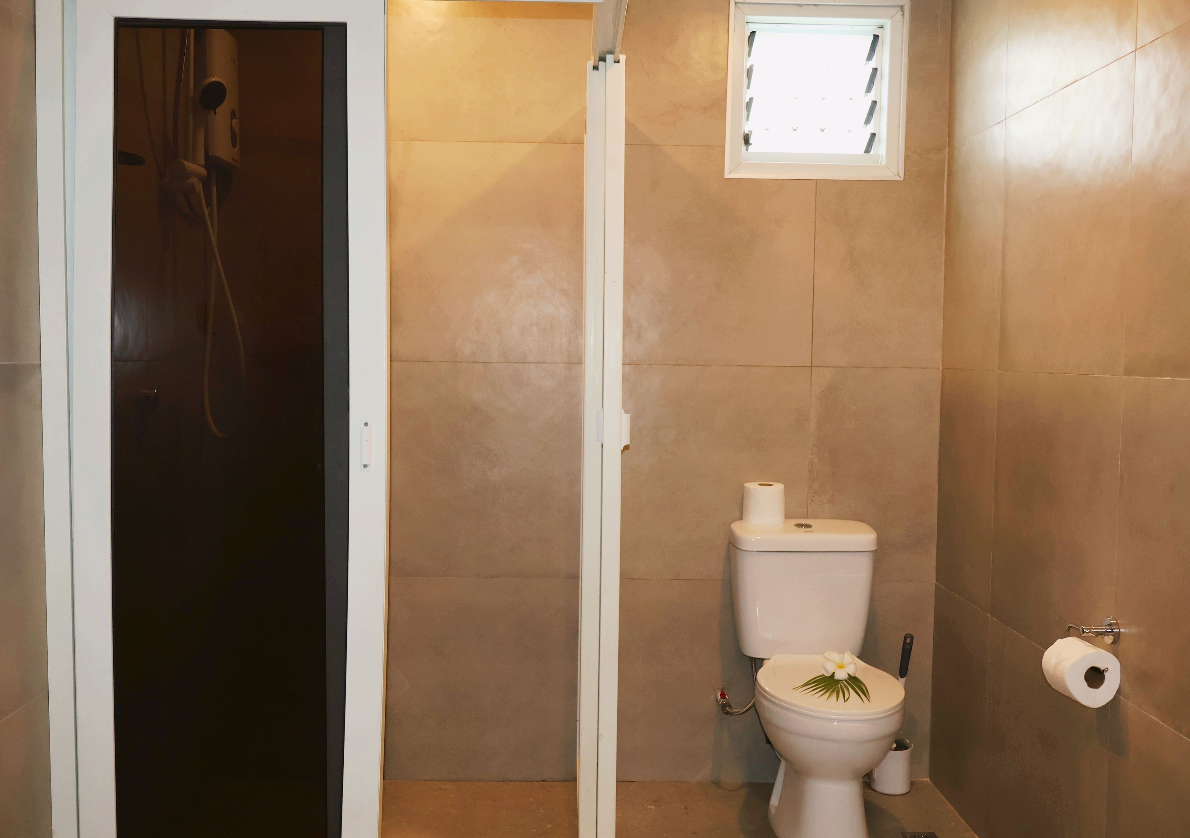 Une salle de bain avec une douche, des toilettes et une petite fenêtre.