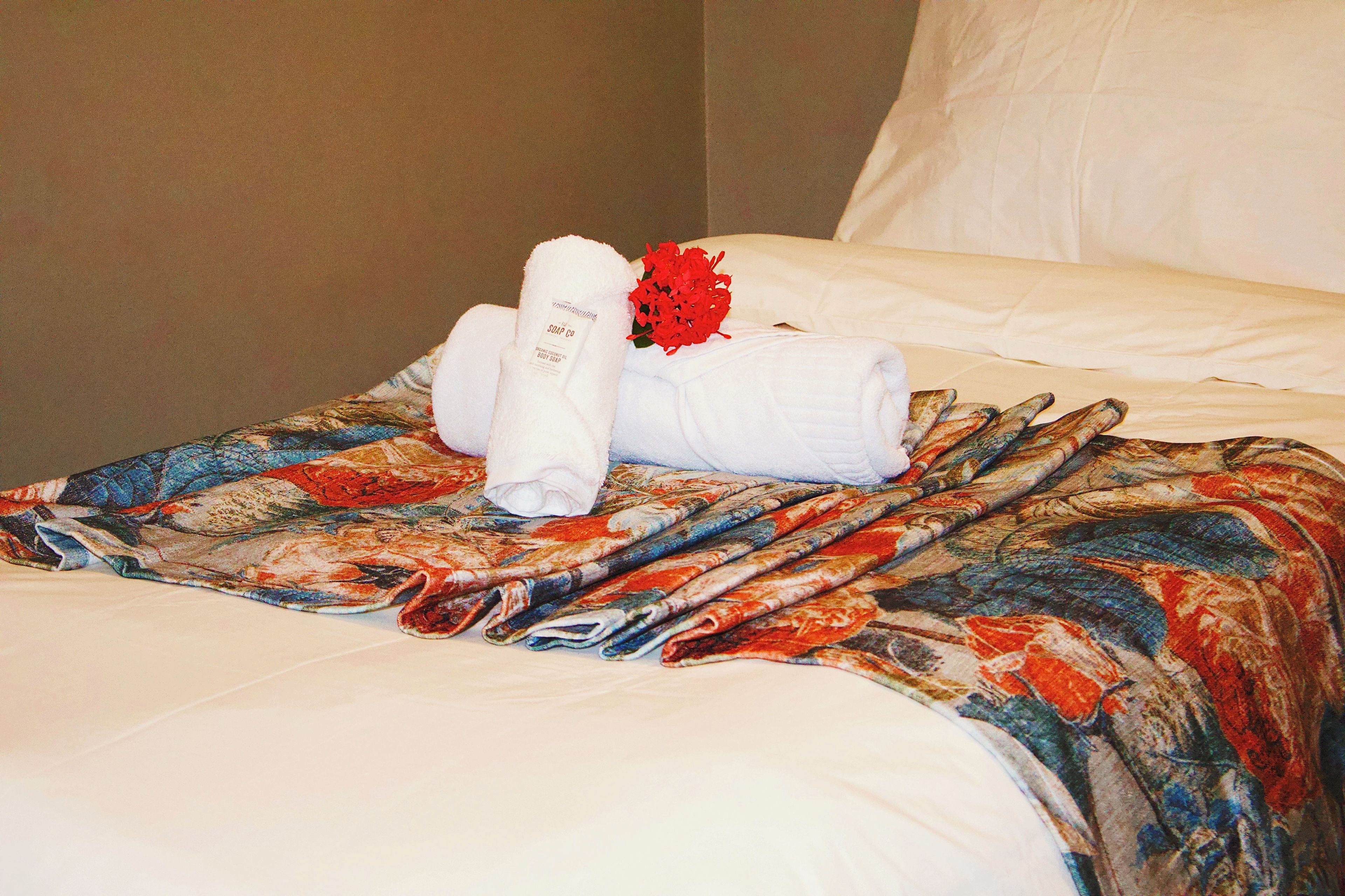 A neatly made bed with a floral-patterned blanket, a white pillow, and a bouquet of red flowers.
