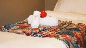 A neatly made bed with a floral-patterned blanket, a white pillow, and a bouquet of red flowers.