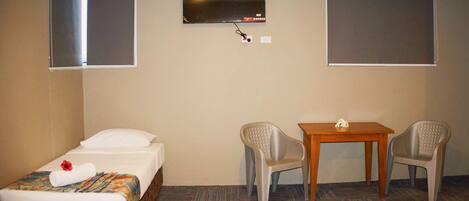 Habitación de hotel con una cama individual, una mesita, dos sillas y un televisor montado en la pared.