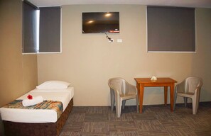 Ein Hotelzimmer mit einem Einzelbett, einem kleinen Tisch, zwei Stühlen und einem an der Wand befestigten Fernseher.