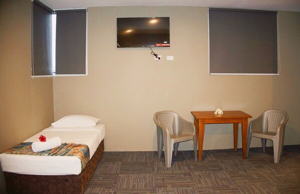Habitación de hotel con una cama individual, una mesita, dos sillas y un televisor montado en la pared.