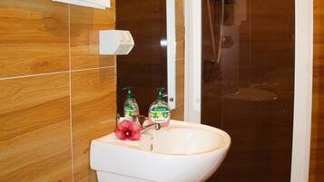 A bathroom with a white sink, two bottles of liquid soap, a mirror, and a shower enclosure.